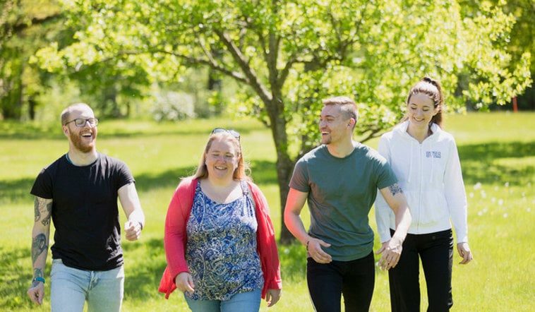 Fyra personer går över en park och pratar.